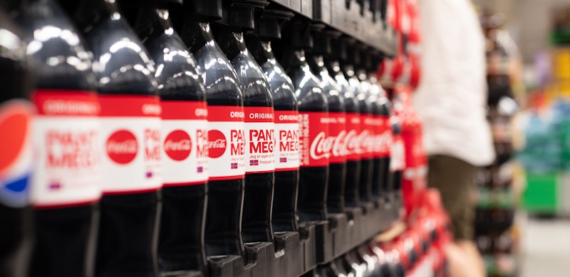 Dette blir billigere fra 1. juli Palle med Coca Cola (med og uten sukker) i butikk. I bakgrunnen skimtes en handlende person. Foto.