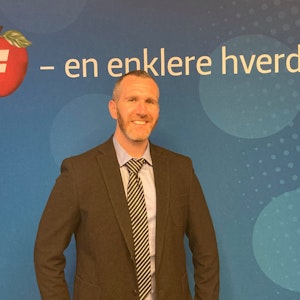 Marius A. Nilsen. Smilende i skjorte, slips og mørk dressjakke, foran en blå vekk merket med FrP logo og påskriften "en enklere hverdag". Foto.