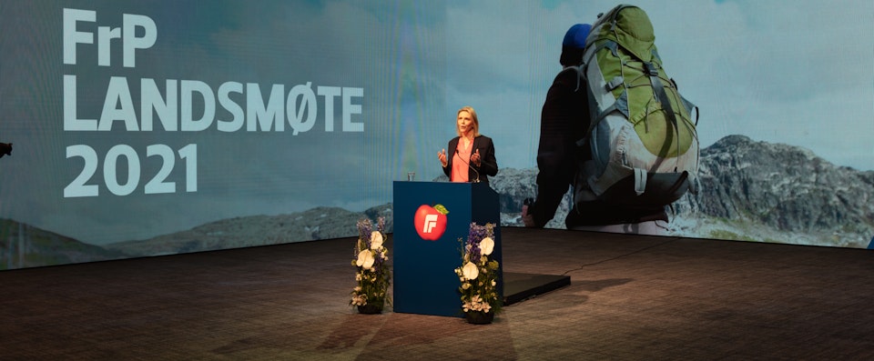 Sylvi Listhaug på talerstolen på FrPs landsmøte i 2021. Bak henne en LED-skjerm med bilde av en turgåer med grønn sekk.