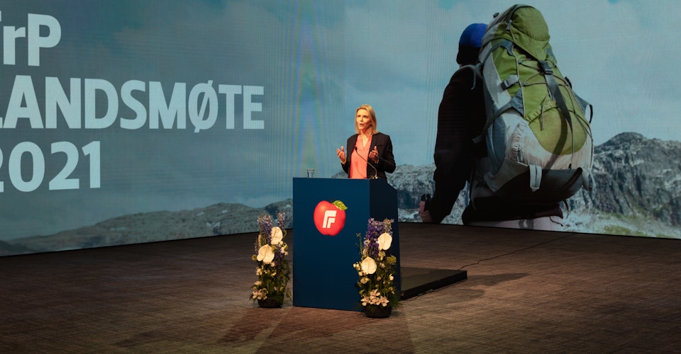 Sylvi Listhaug på talerstolen på FrPs landsmøte i 2021. Bak henne en LED-skjerm med bilde av en turgåer med grønn sekk.