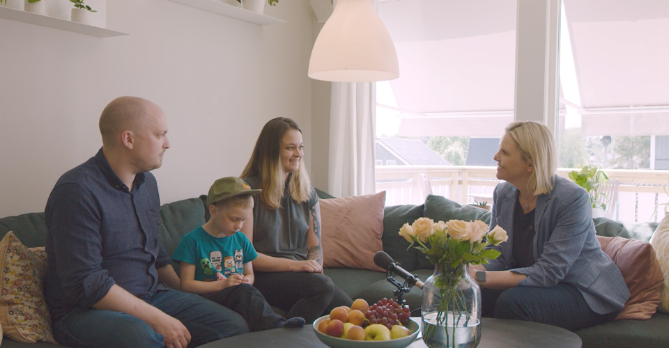 Sylvi Listhaug i en stor sofa sammen med familien Jønsson. De prater sammen. På bordet foran en bukett blomster og et fat med frukt. Foto.