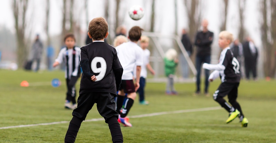 Flere barn i sorte og hvite drakter som spiller fotball utendørs. Foto.
