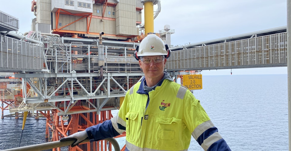 Ketil Solvik-Olsen på oljeplattform, som kan sees i bakgrunnen. Iført refleksjakke og hjelm. Foto.