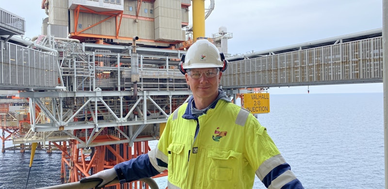 Ketil Solvik-Olsen på oljeplattform, som kan sees i bakgrunnen. Iført refleksjakke og hjelm. Foto.