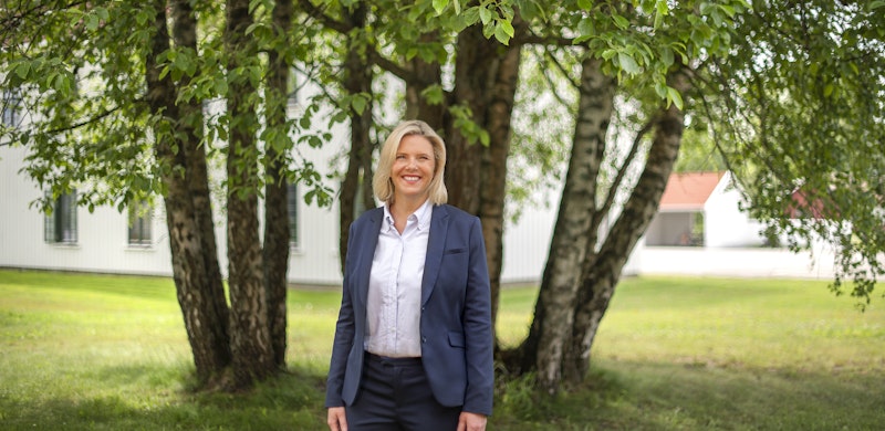 Sylvi Listhaug, smilende ikledd dressjakke. I bakgrunnen grønne trær. Foto.