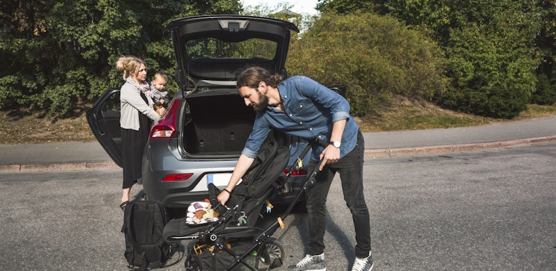 Familie med lite barn som er på vei til å pakke barnevognen inn i en stasjonsvogn. Foto.